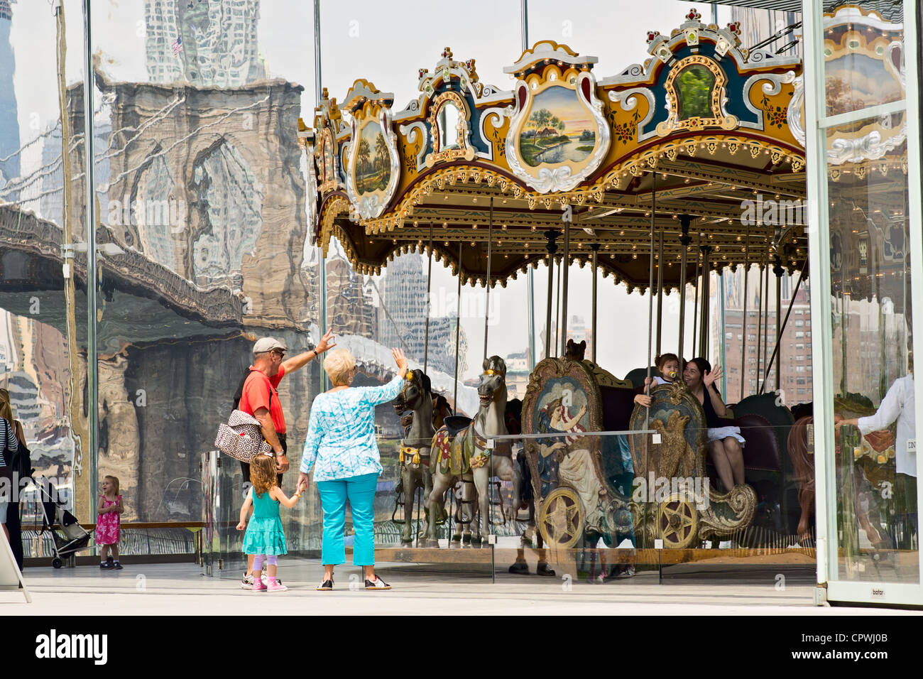 Vieux couple avec jeune enfant vague à personnes sur Jane's Carousel, pont de Brooklyn Park, Brooklyn, NY, US Banque D'Images