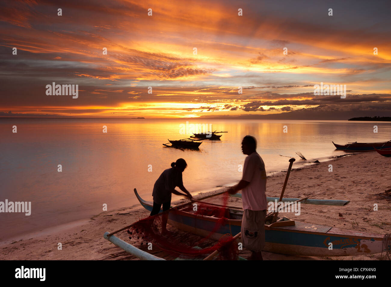 Pêcheur & woman tending moustiquaires au crépuscule sur la plage de San Juan, les Visayas, Siquijor, Philippines Banque D'Images