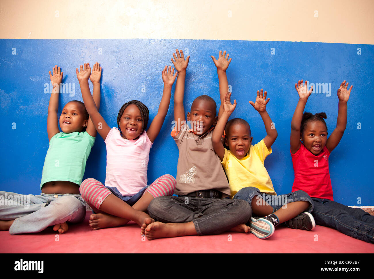 Cinq enfants assis contre un mur avec leurs mains en l'air Banque D'Images
