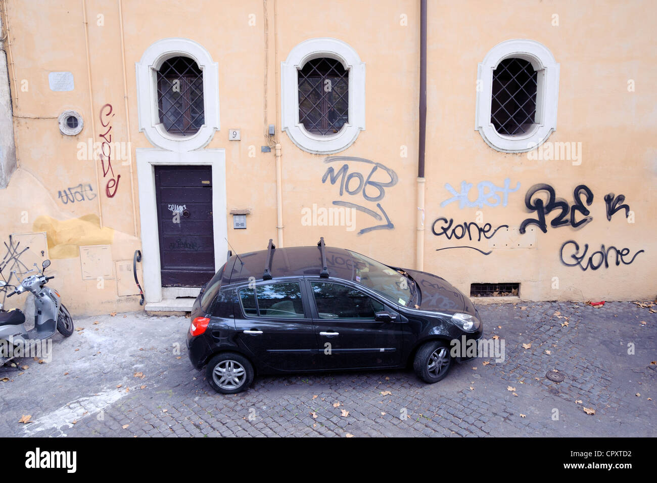 Petite voiture noire garée devant une maison couverts de graffiti à Rome. Banque D'Images
