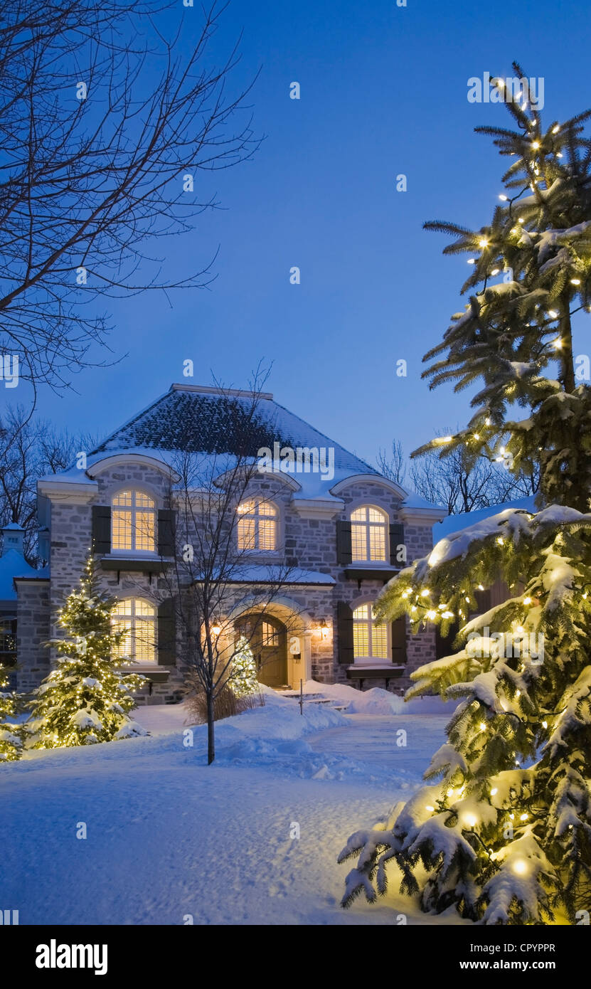 Chalet luxueux de style résidentiel maison avec les arbres à feuilles persistantes illuminée au crépuscule en hiver, Québec, Canada Banque D'Images