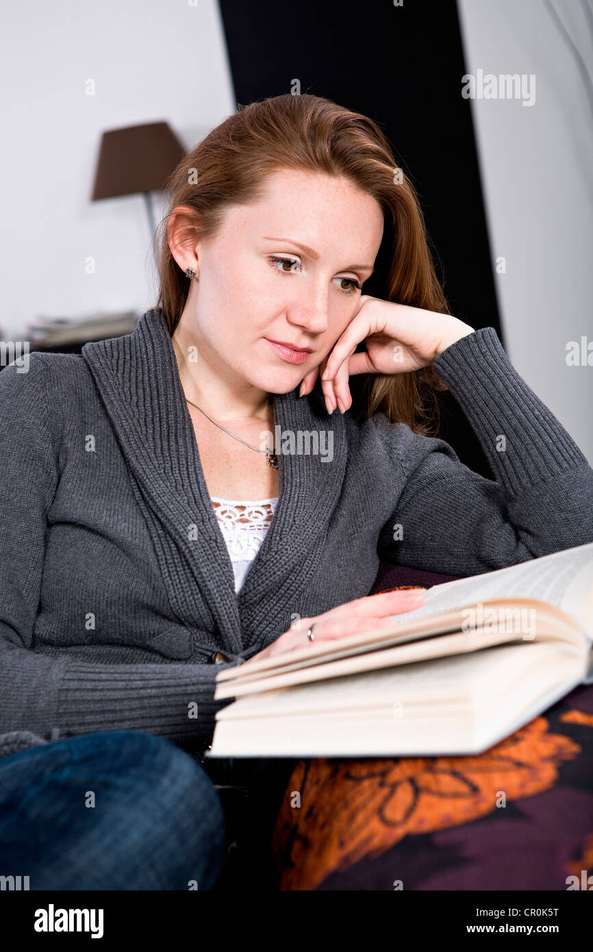 Jeune femme lisant un livre dans le salon Banque D'Images