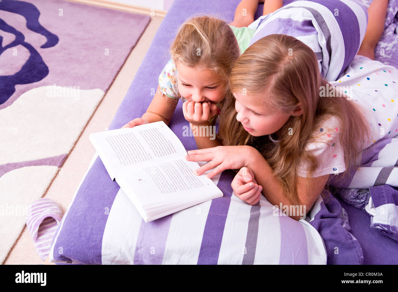 Deux jeunes filles, sœurs lire au lit Banque D'Images