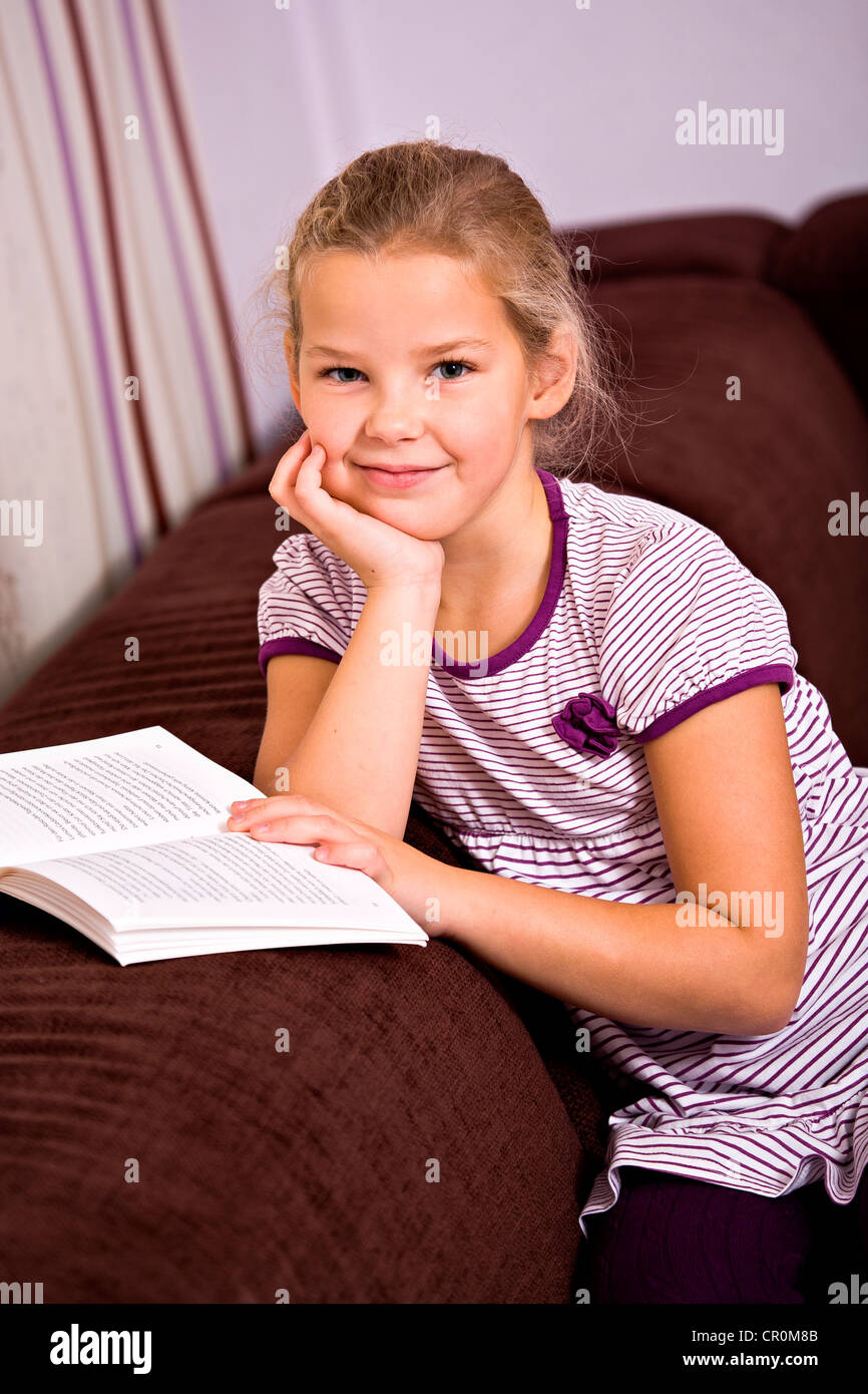 Fille, 8, assis sur un canapé avec un livre Banque D'Images