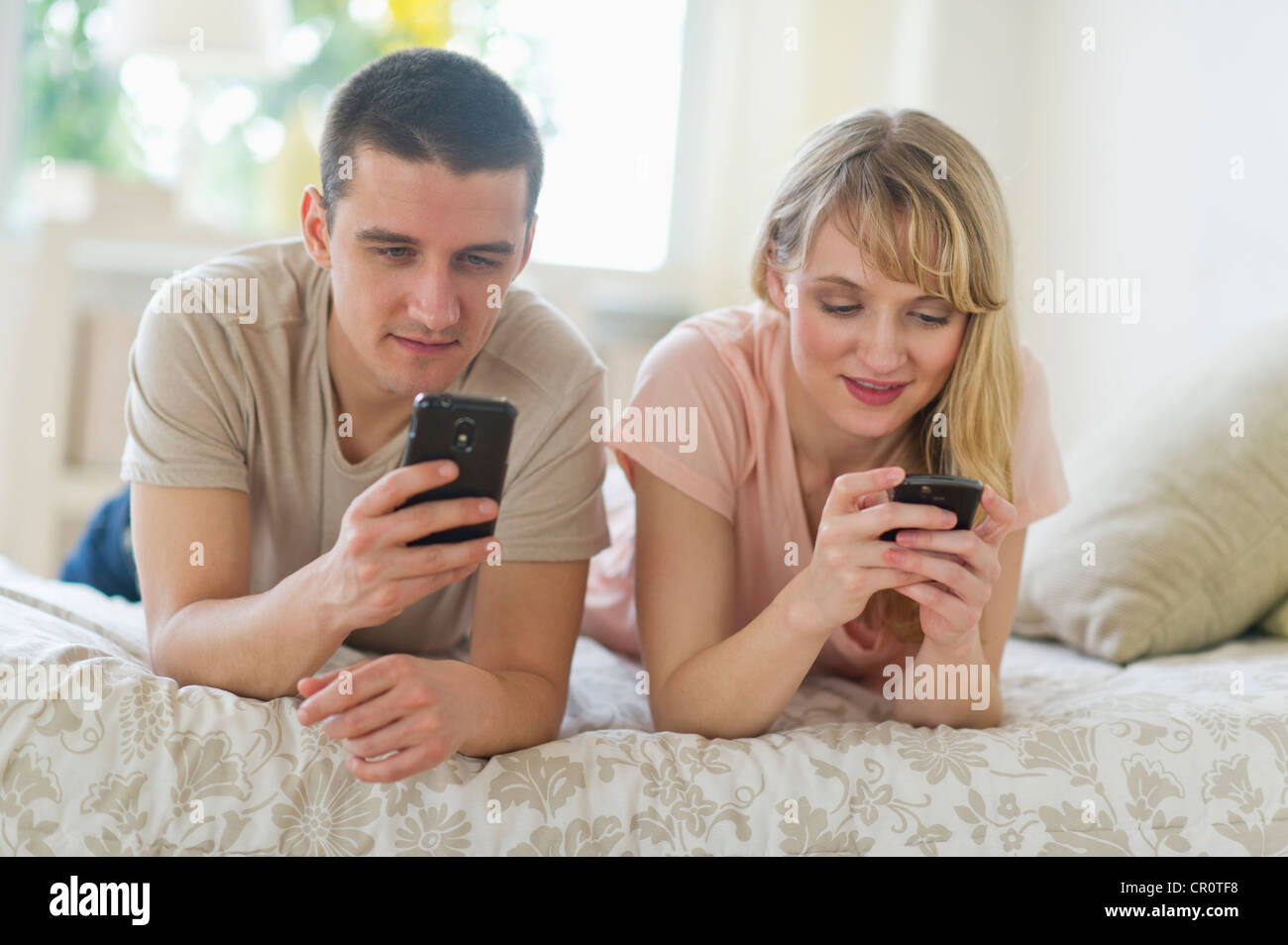 USA, New Jersey, Jersey City, Couple lying on bed et avec les téléphones intelligents Banque D'Images