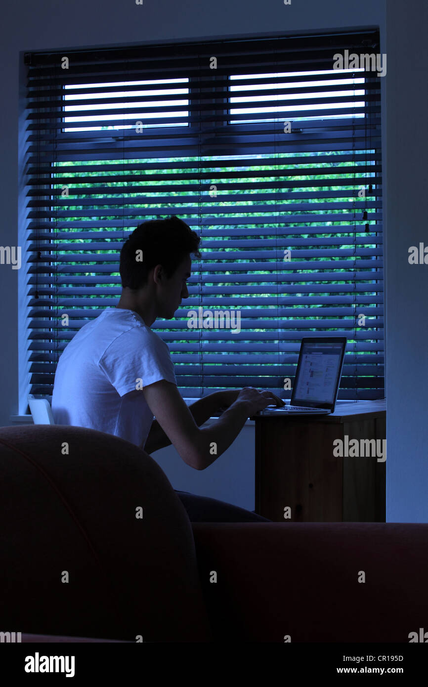 Jeune homme assis dans une pièce sombre à l'aide d'un ordinateur portable. Banque D'Images