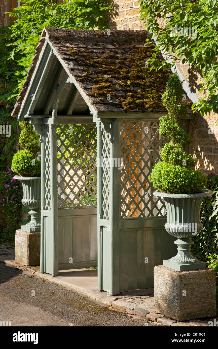 Véranda en bois avec des côtés de Cotswold cottage flanquée de fort topiaire en spirale dans les urnes en pierre, en Angleterre Banque D'Images