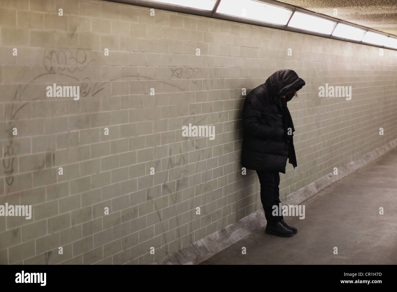 Personne à capuchon s'appuyant sur le mur du métro Banque D'Images