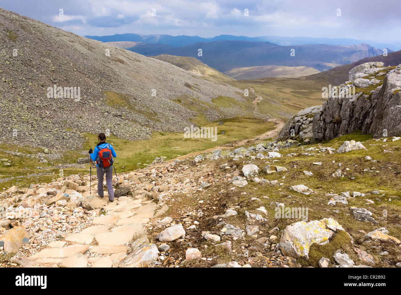Un randonneur descend le chemin escarpé des sommets de mauvais et Broad Crag dans le Lake District. Le Langdale Pikes peut être vu dans le Banque D'Images