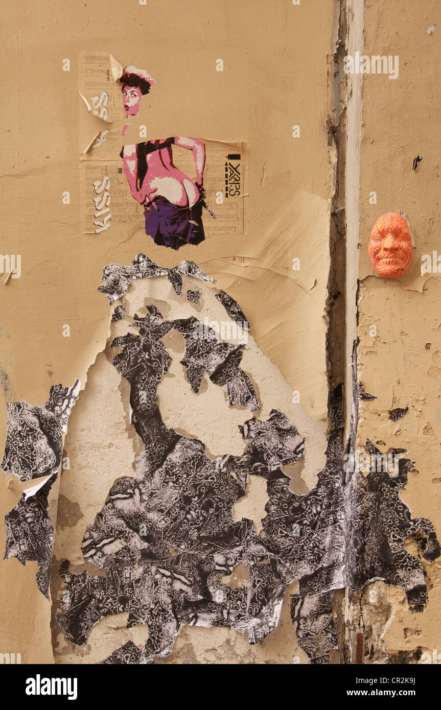 Un détail de déchiré, pealing affiches et un masque peint de couleurs vives, collé sur un mur texturé gros découvert dans une ruelle parisienne. Paris, France. Banque D'Images