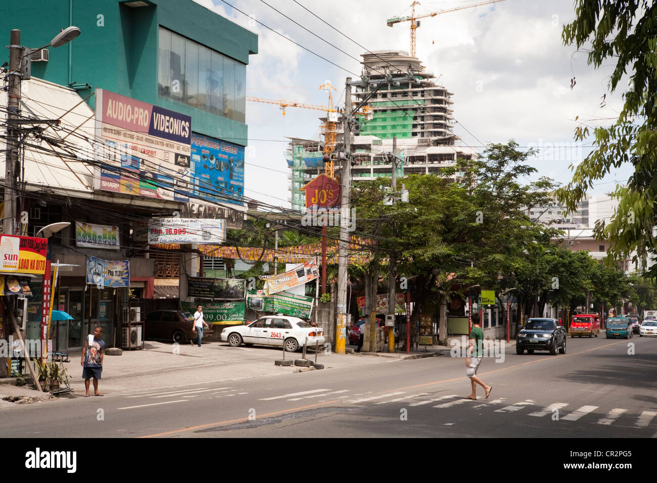 L'homme de traverser la route, la construction de gratte-ciel en construction à l'arrière-plan fait partie d'Asiatown IL Park. La ville de Cebu, Cebu.. Banque D'Images