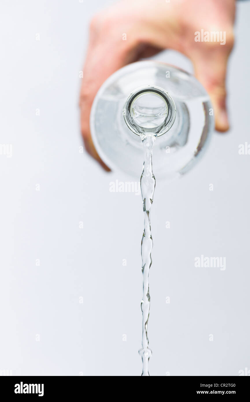 Verser l'eau minérale de la main une bouteille en verre contre fond blanc Banque D'Images