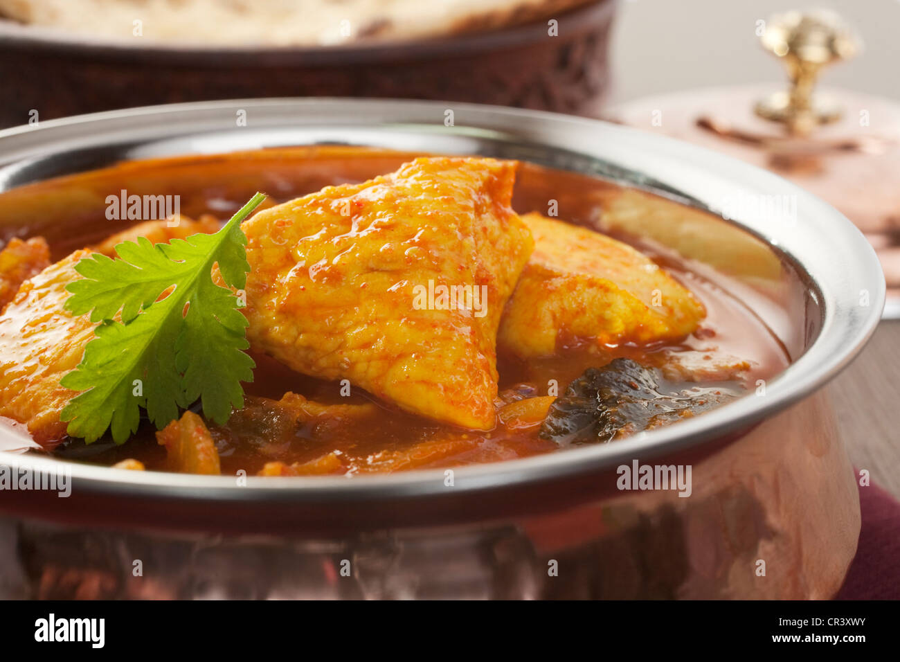 Poulet madras curry dans un bol de cuivre, avec du pain naan en arrière-plan. Banque D'Images