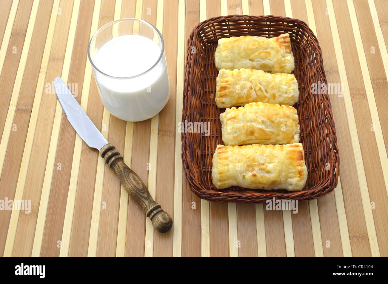 Pâtisseries maison, pâte feuilletée remplie dans un panier petit-déjeuner à côté d'un couteau à beurre et un verre de lait Banque D'Images