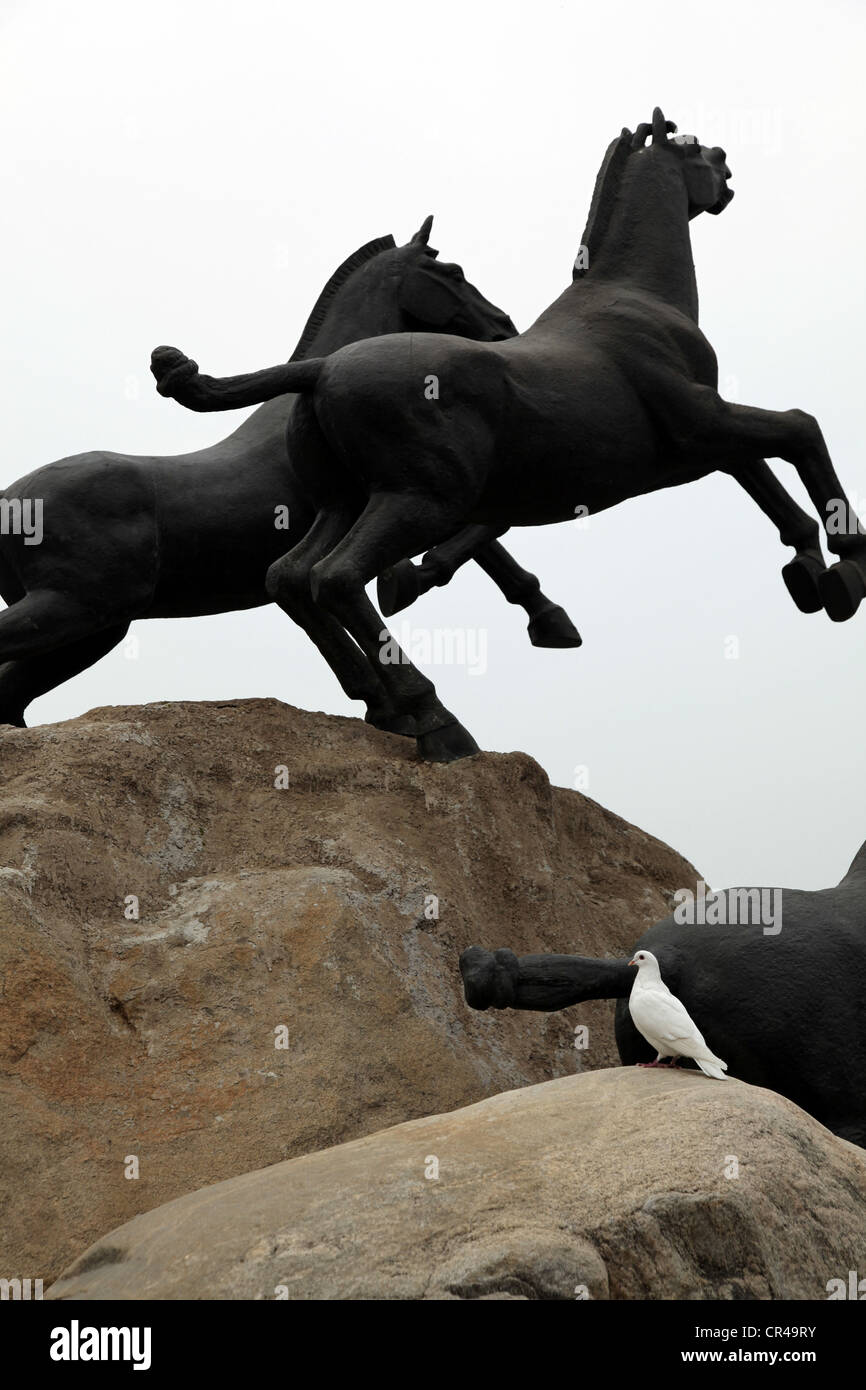 C'est une photo de statues de chevaux faits à partir du fer ou d'acier ou de cuivre. Ils sont debout sur un gros rocher au milieu d'une ville. Ils courent Banque D'Images