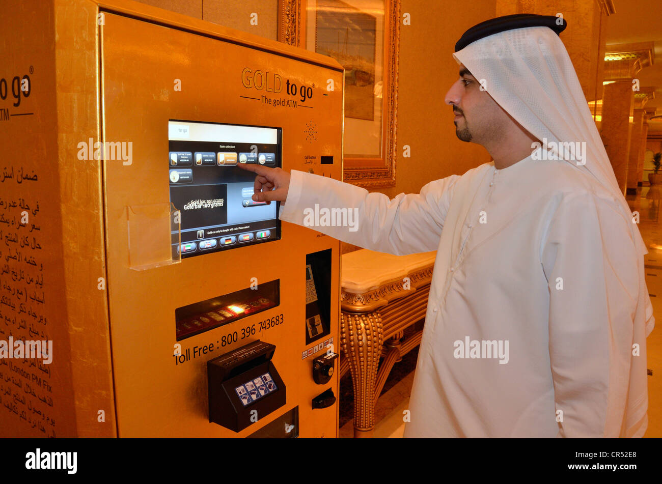 Homme portant une dishdasha locale, traditionnelle robe blanche, en face de la machine or 'or to go' dans l'Emirates Palace Hotel Banque D'Images