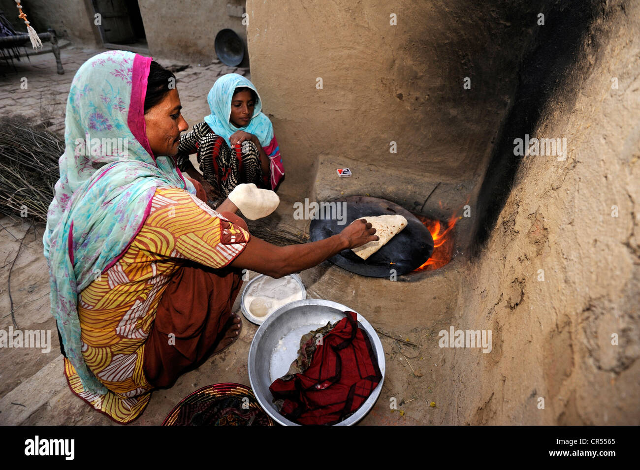 Femme et fille la cuisson du pain sans levain traditionnel, chapati, sur un simple four en argile, ils vivent et travaillent avec leur famille sous Banque D'Images