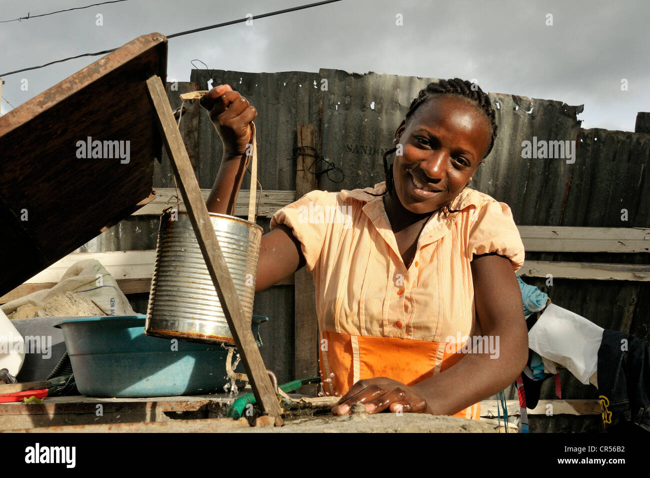 Jeune femme à la peau sombre de l'extraction de l'eau d'un puits dans une boîte, Port-au-Prince, Haïti, Caraïbes, Amérique Centrale Banque D'Images