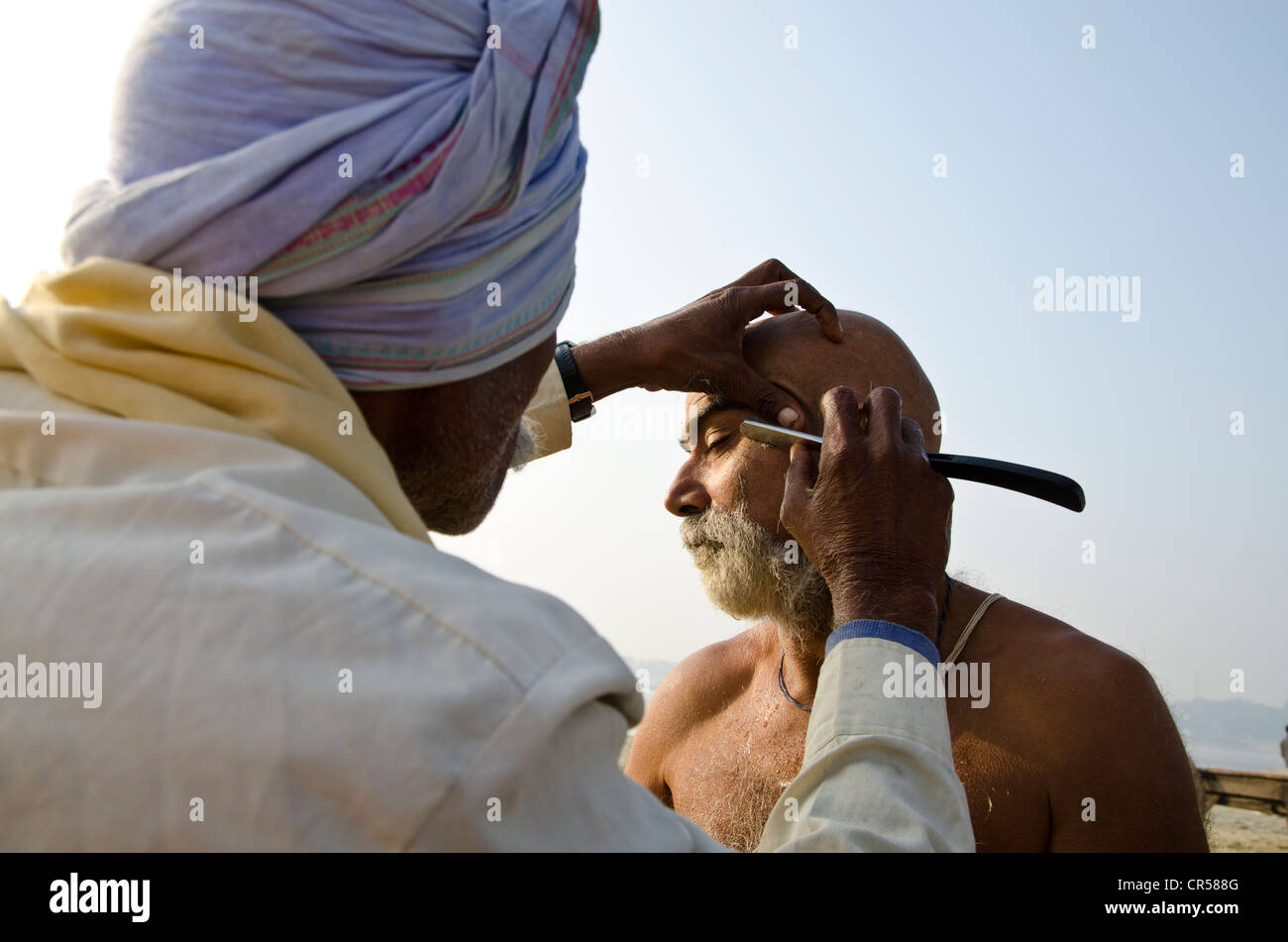 La tête de rasage dans le cadre d'un rituel religieux, effectuée à Sangam, la confluence des rivières saint Ganges Banque D'Images