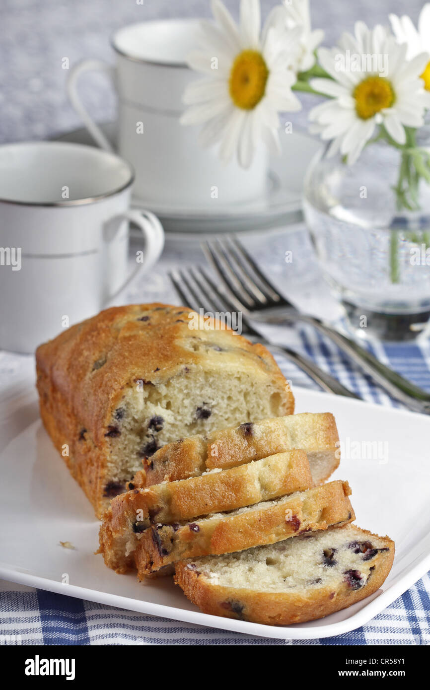 Un pain en tranches de pain aux bleuets avec 2 tasses à café et soucoupes et des marguerites Shasta sur une nappe à rayures bleu et. Banque D'Images