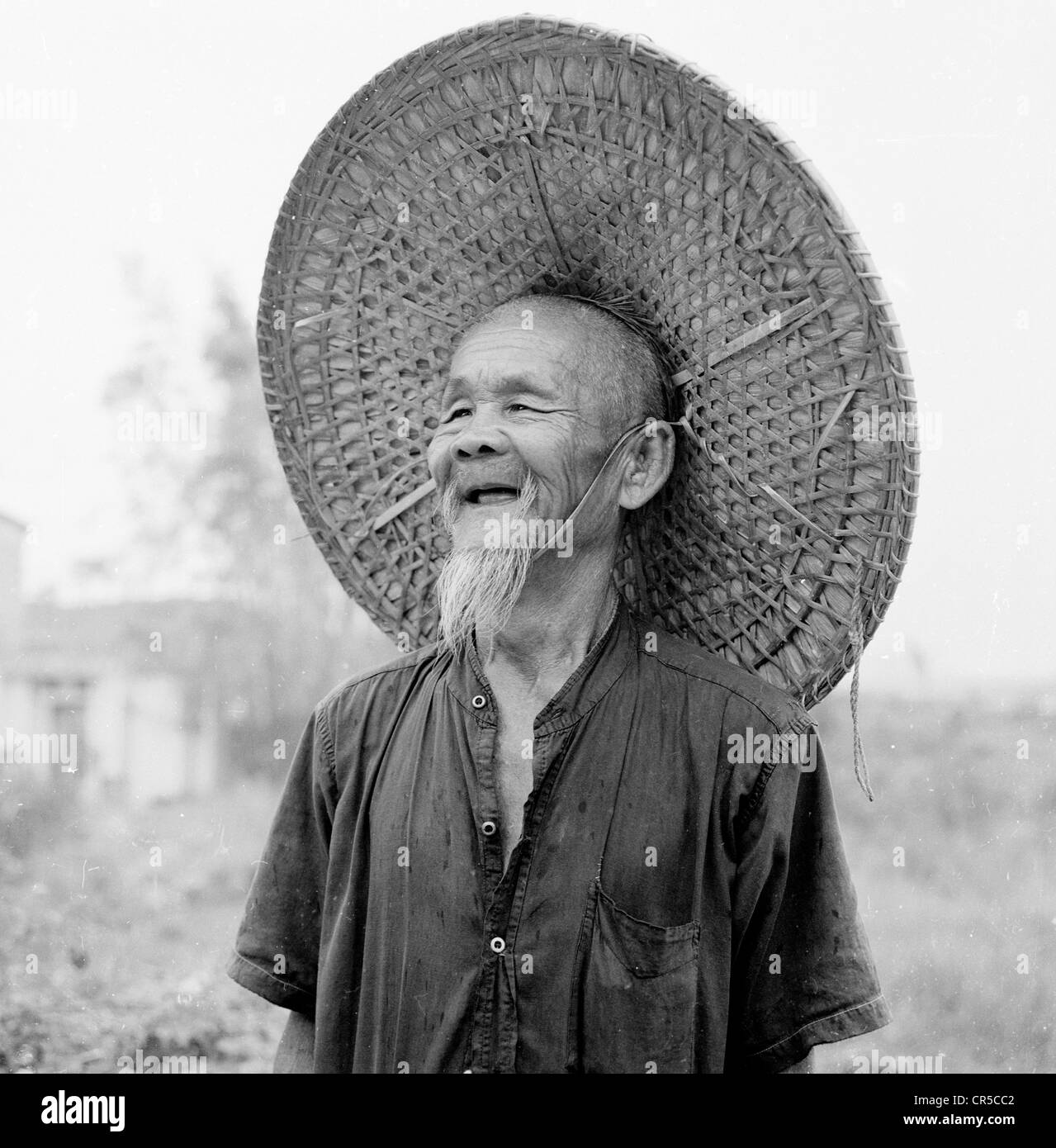 Hong Kong, 1950. Un homme âgé travailleur chinois en costume traditionnel, portant une large wicker rond ou conique coolie hat. Banque D'Images