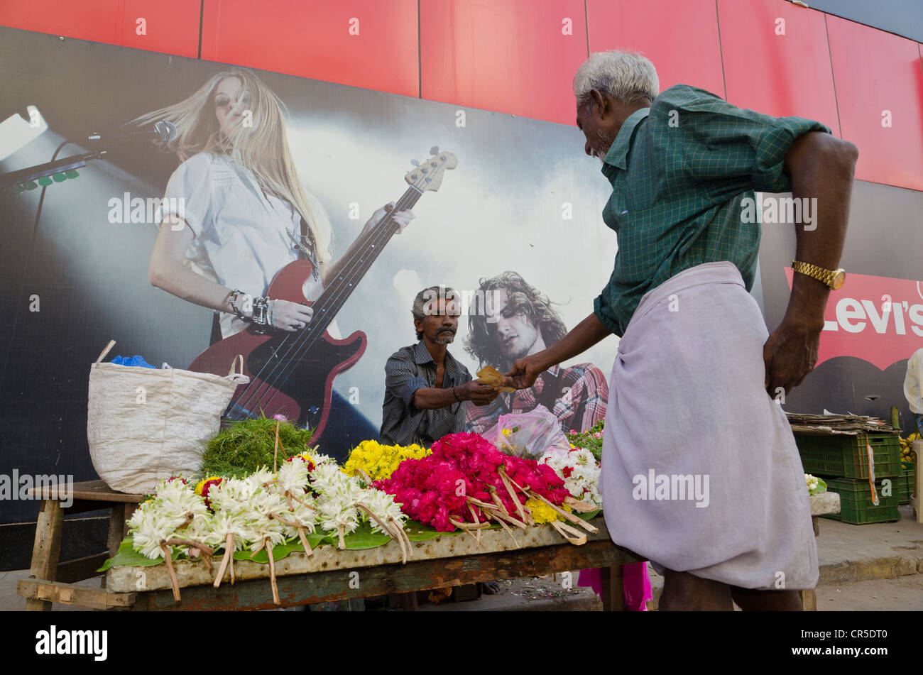Flowerseller avec sa boutique mis en place en face d'une affiche de concert, Madurai, Tamil Nadu, Inde, Asie Banque D'Images
