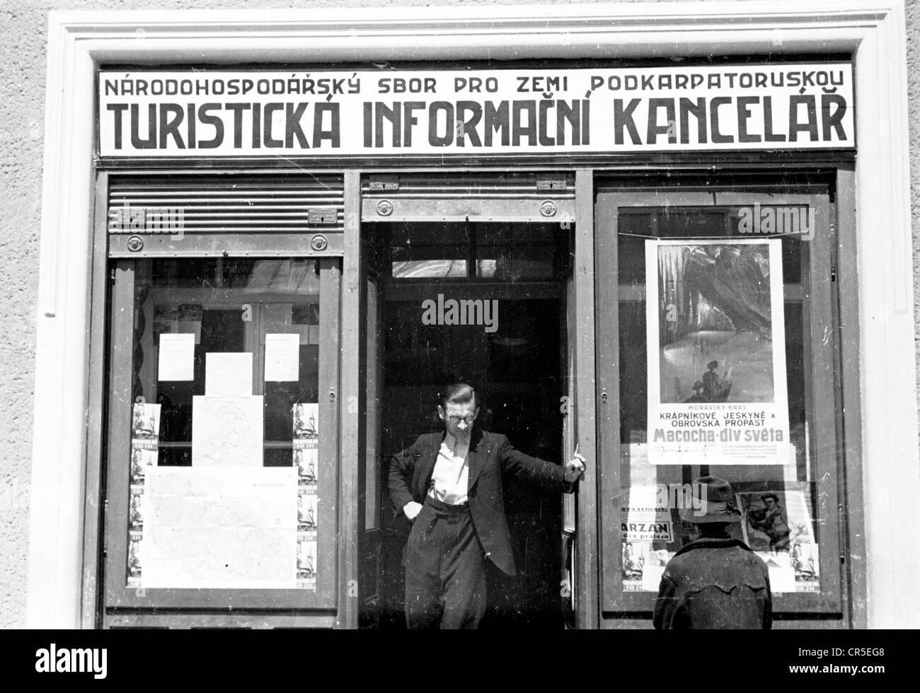 1930s, historique, la Tchécoslovaquie d'avant-guerre, un homme debout à la porte d'un bureau d'information des premiers visiteurs, Turisticka Informacni Kancelar dans cette photo prise par J Allan Cash, qui a visité l'Europe de l'est à cette époque. Une affiche pour Macocha -div Sevta est affichée dans la fenêtre. Banque D'Images