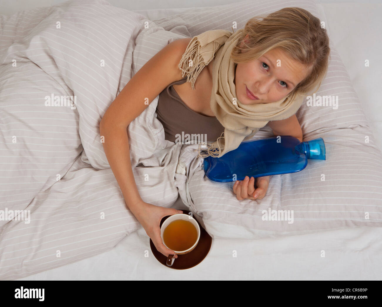 Teenage girl lying on bed with hot water bottle et tasse de thé Banque D'Images