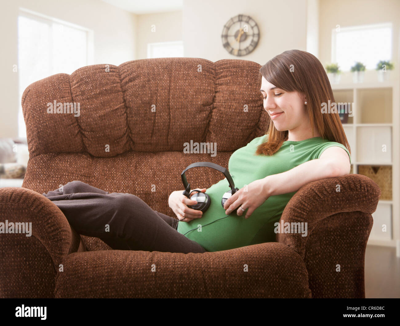 Portrait of pregnant woman sitting on sofa avec un casque sur son ventre Banque D'Images