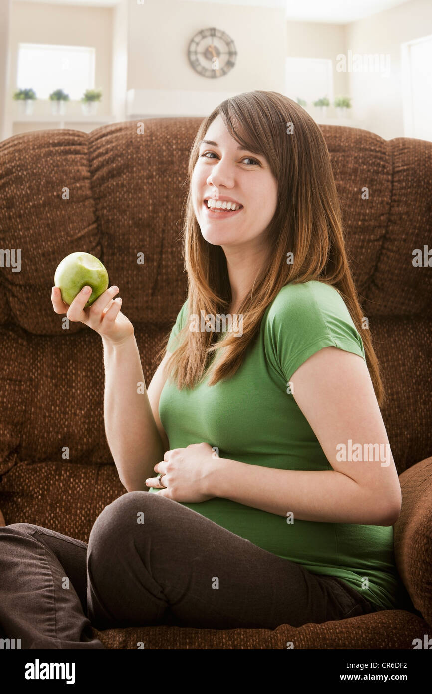 Portrait of pregnant woman sitting on sofa and eating apple Banque D'Images