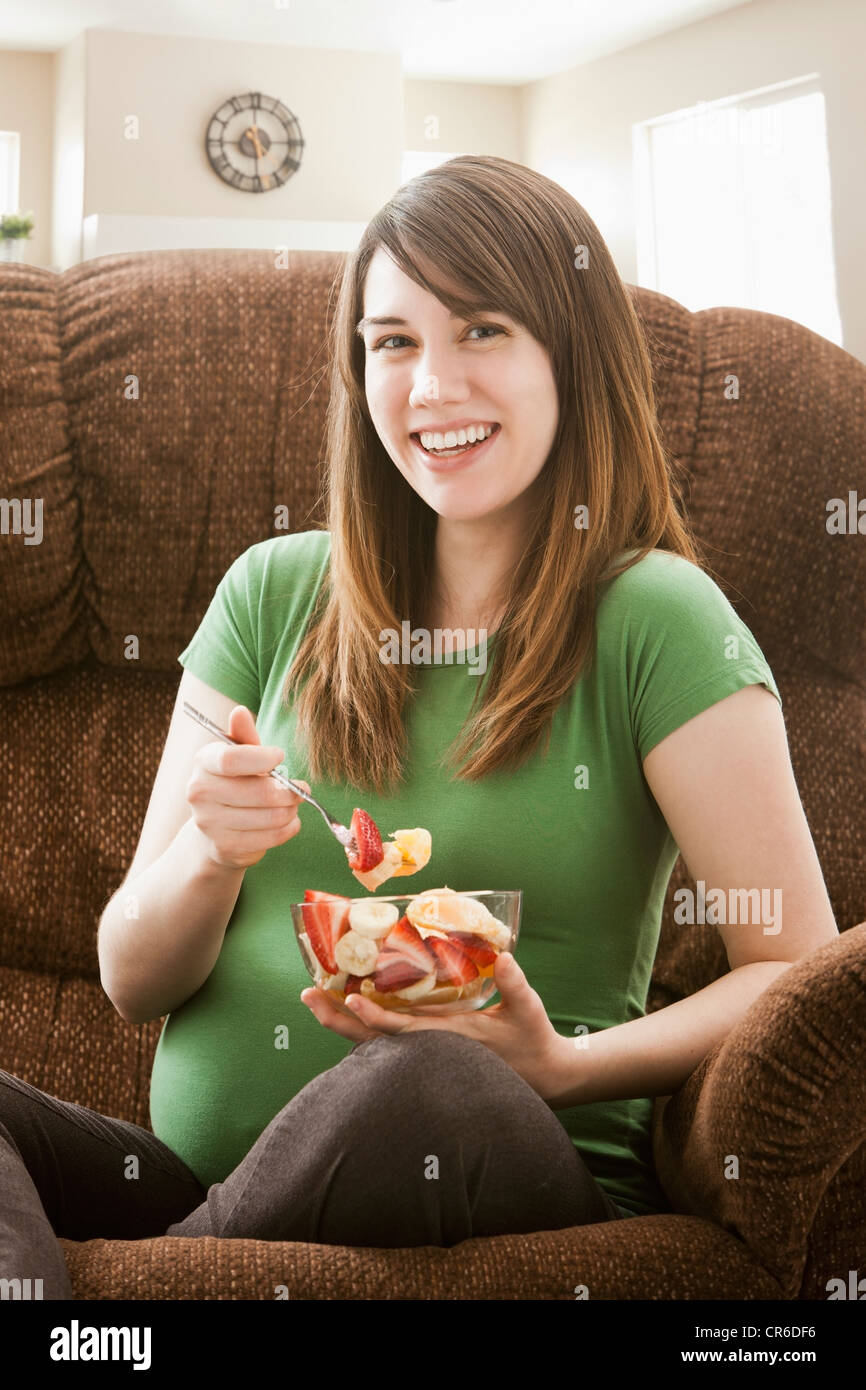 Portrait of pregnant woman sitting on sofa and eating salad Banque D'Images