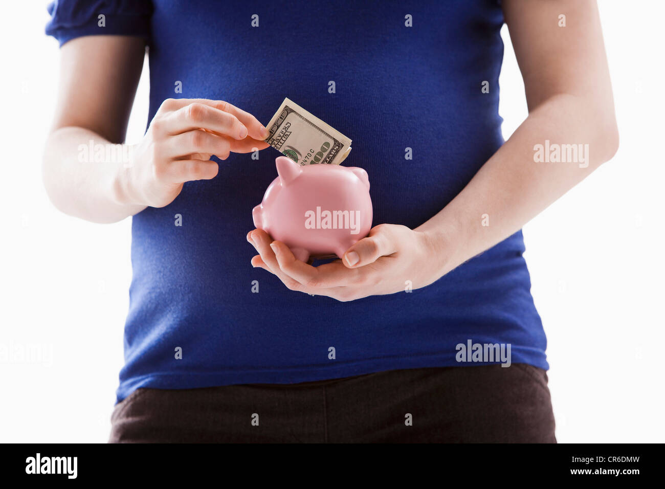 Studio Shot of mid section of pregnant woman putting money into Piggy Bank Banque D'Images