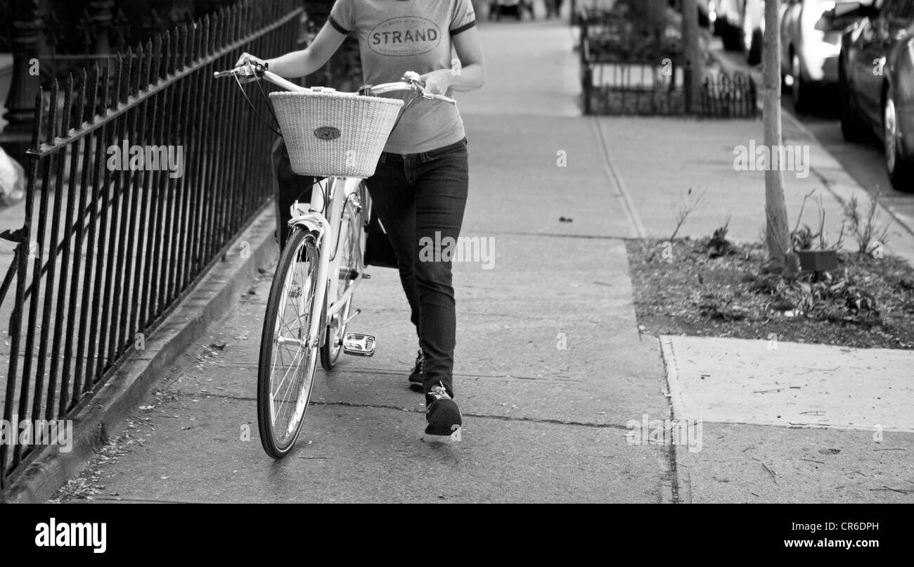 Une femme entre son vélo dans le quartier Park Slope de Brooklyn, New York. Banque D'Images