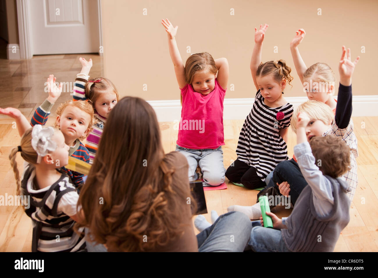 Enfants (2-3, 4-5) sitting on floor et d'élever les mains Banque D'Images