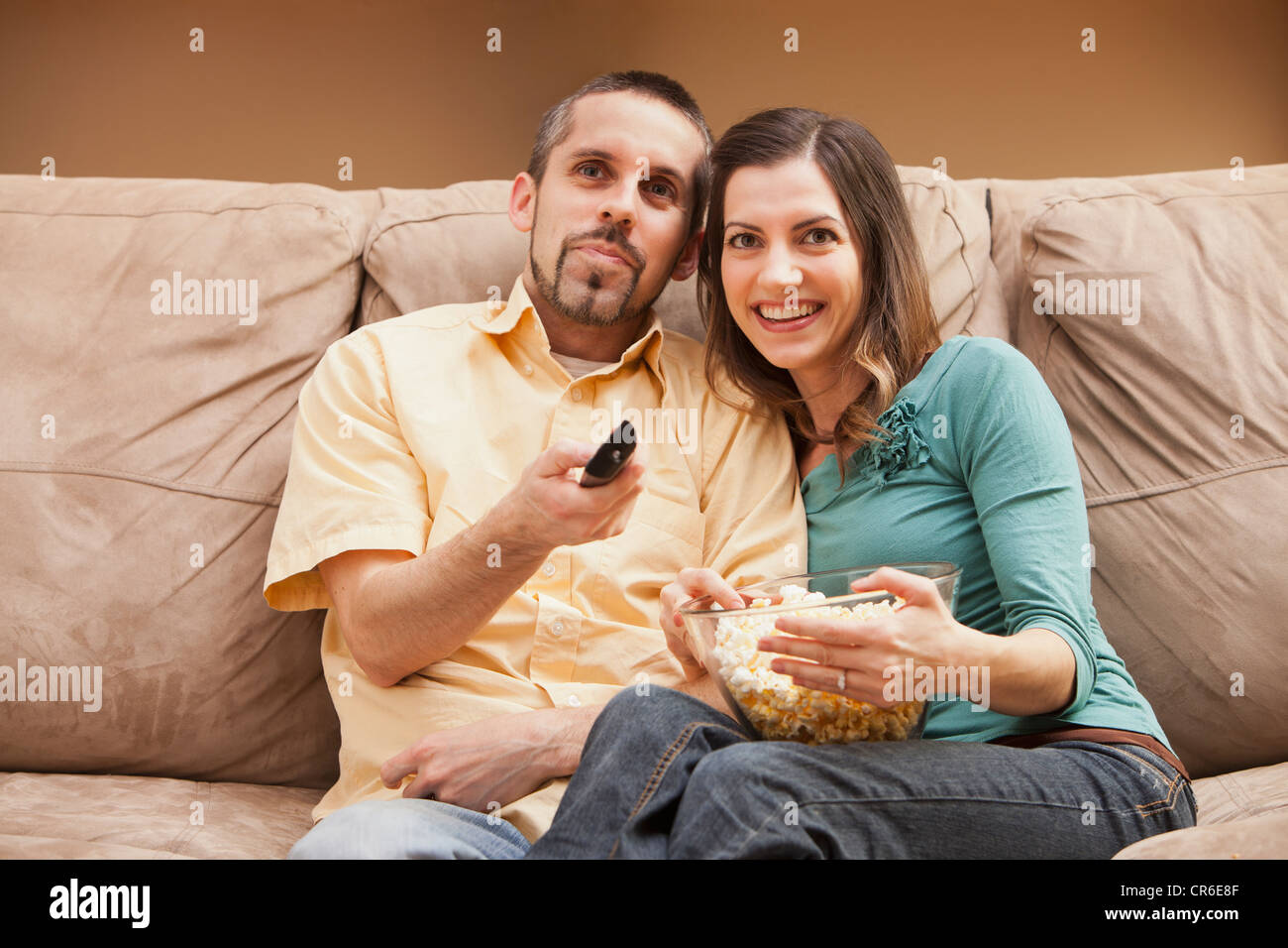 Vue avant du Mid adult couple sitting on couch avec télécommande et du pop-corn Banque D'Images