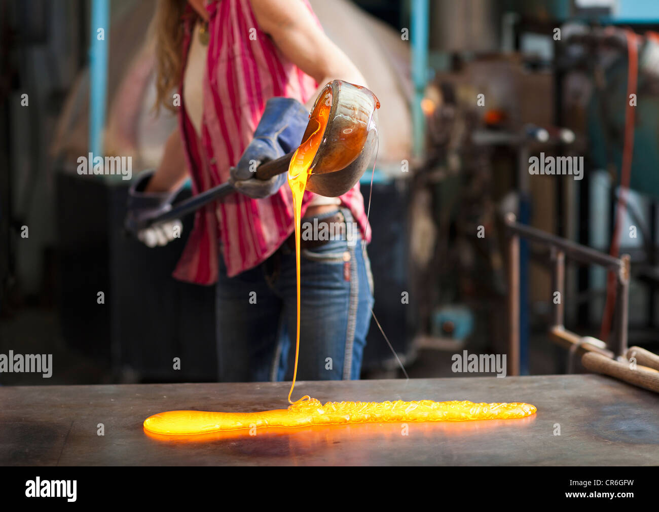 Caucasian woman pouring molten glass in workshop Banque D'Images