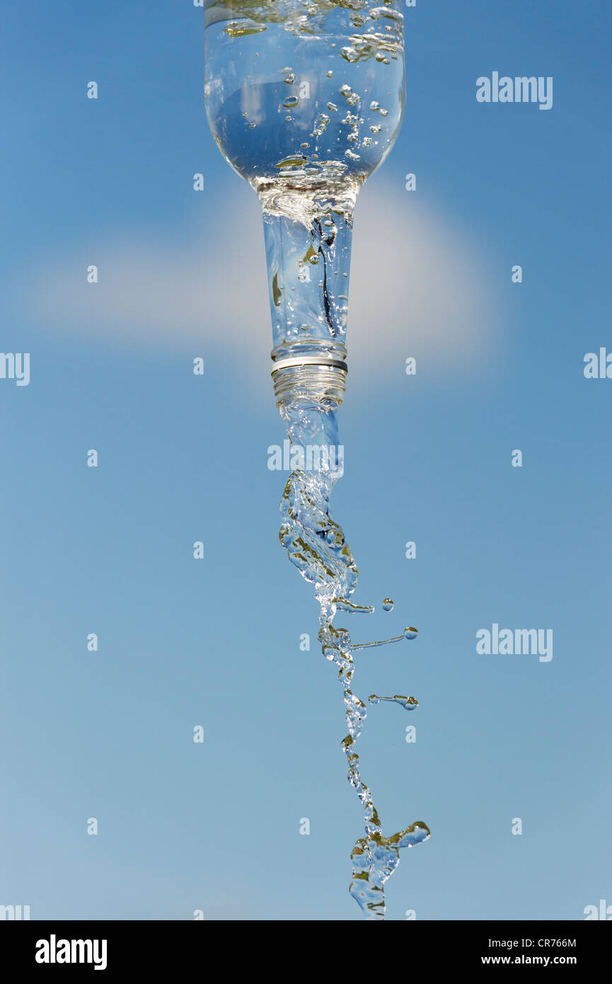 Verser de l'eau potable à partir d'une bouteille de verre contre un ciel bleu Banque D'Images
