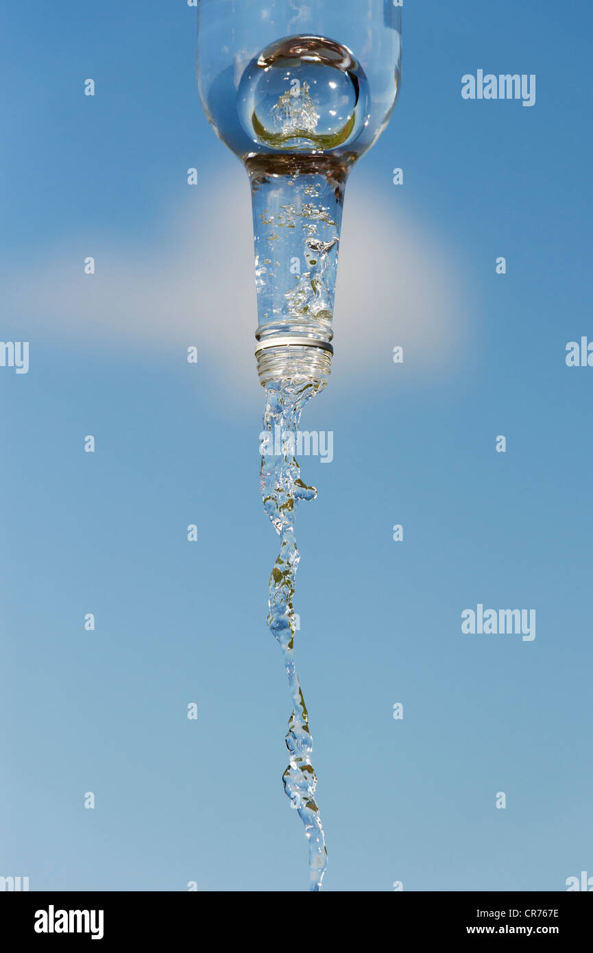 Verser de l'eau potable à partir d'une bouteille de verre contre un ciel bleu Banque D'Images