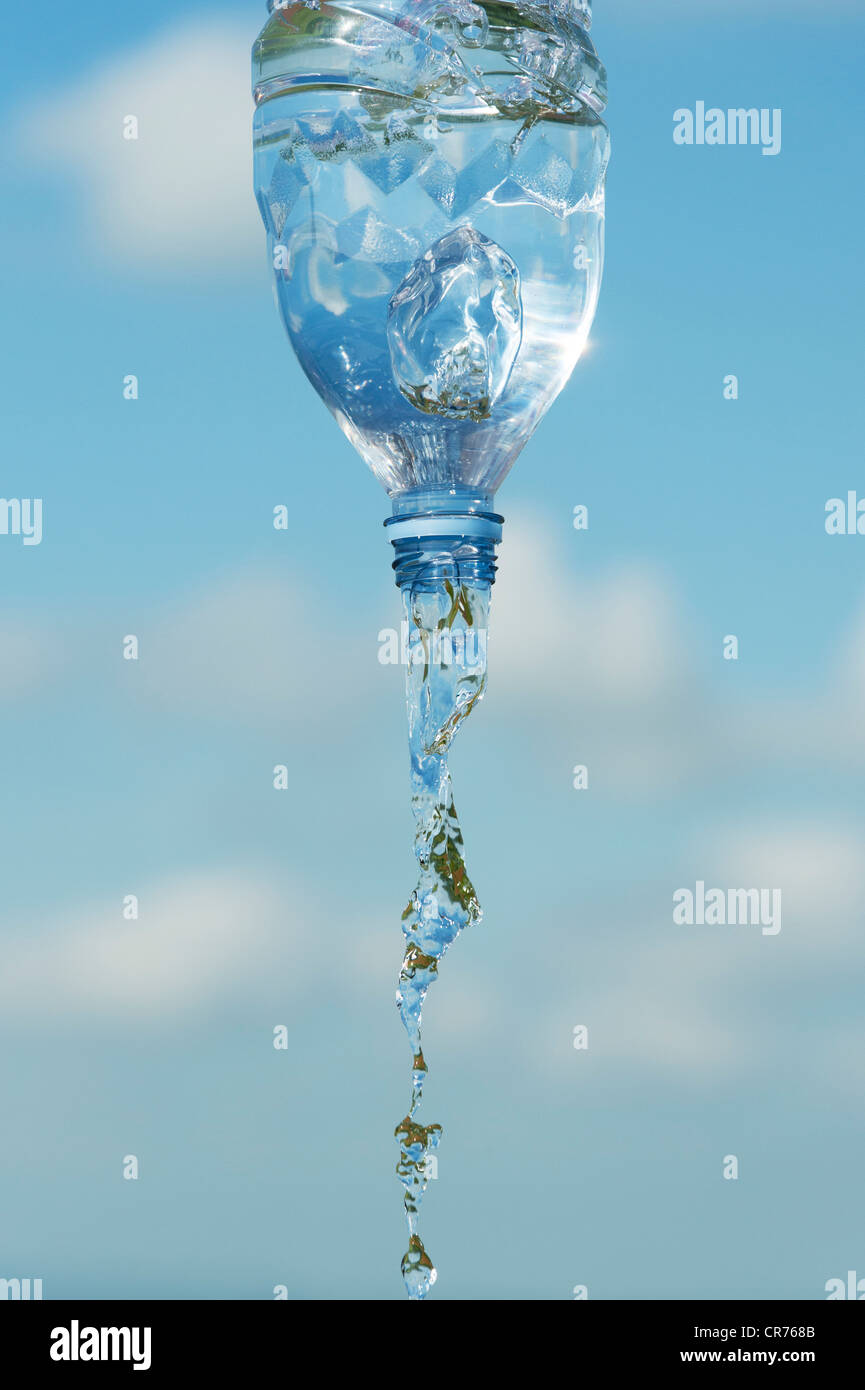 Verser de l'eau potable à partir d'une bouteille en plastique contre un ciel bleu Banque D'Images