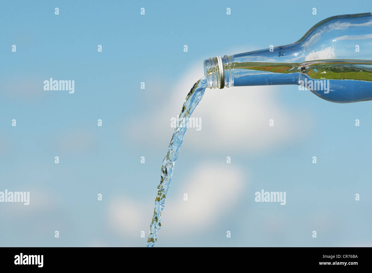 Verser de l'eau potable à partir d'une bouteille de verre contre un ciel bleu Banque D'Images