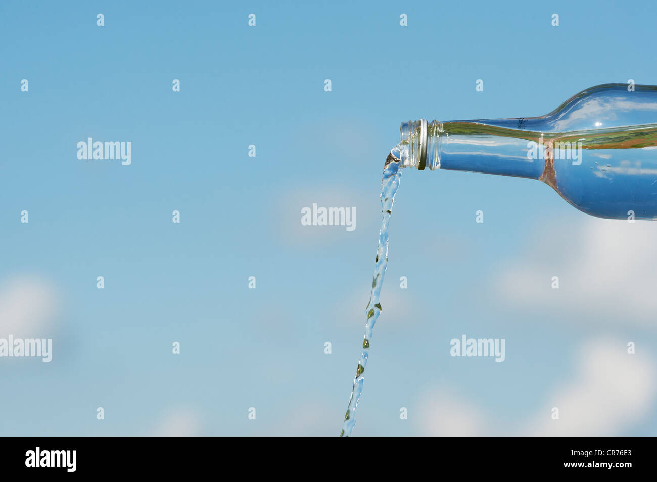 Verser de l'eau potable à partir d'une bouteille de verre contre un ciel bleu Banque D'Images