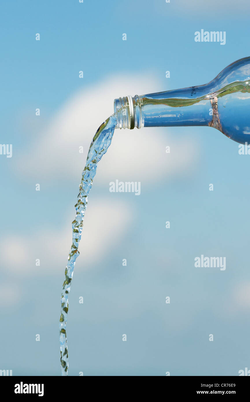 Verser de l'eau potable à partir d'une bouteille de verre contre un ciel bleu Banque D'Images