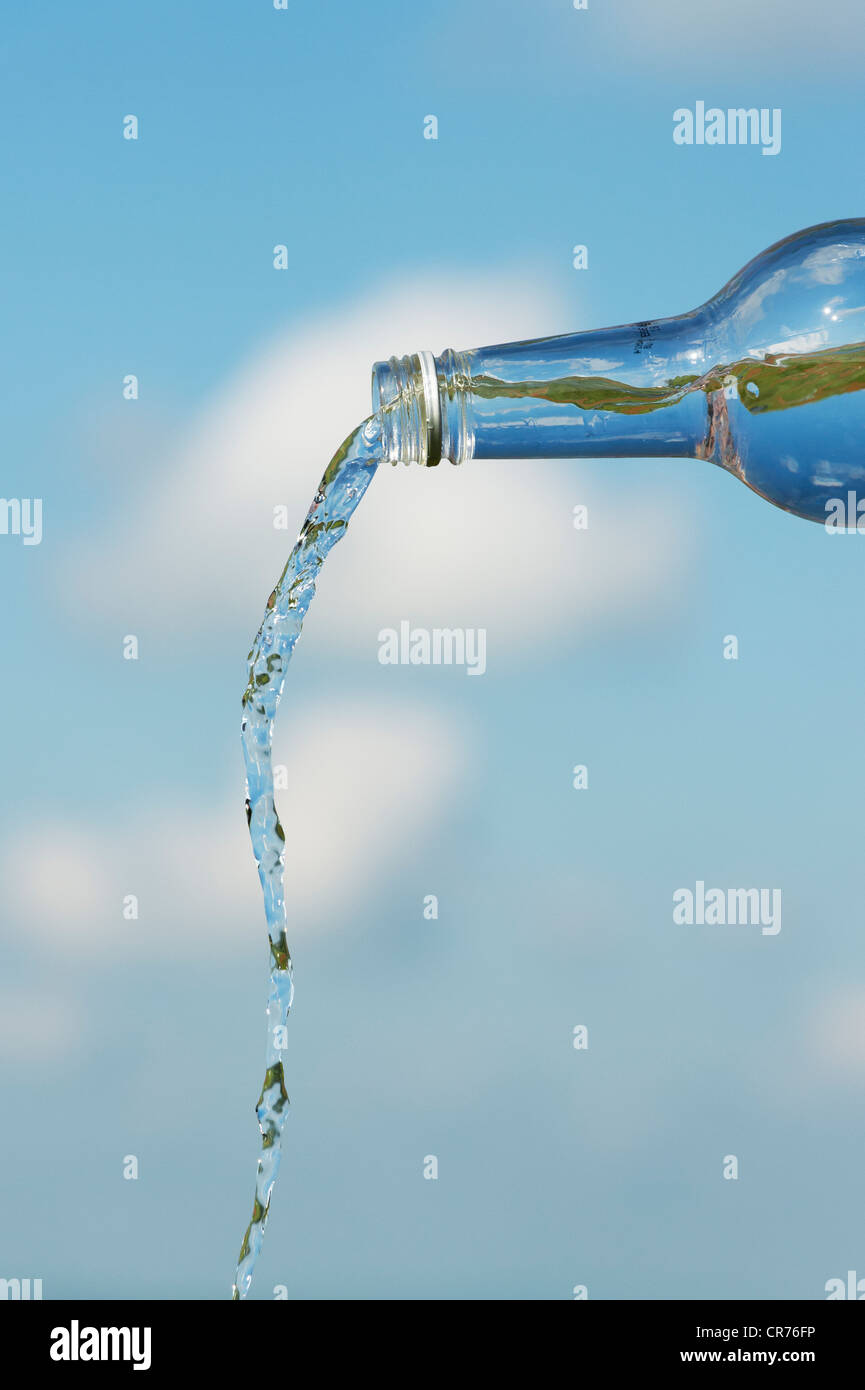 Verser de l'eau potable à partir d'une bouteille de verre contre un ciel bleu Banque D'Images