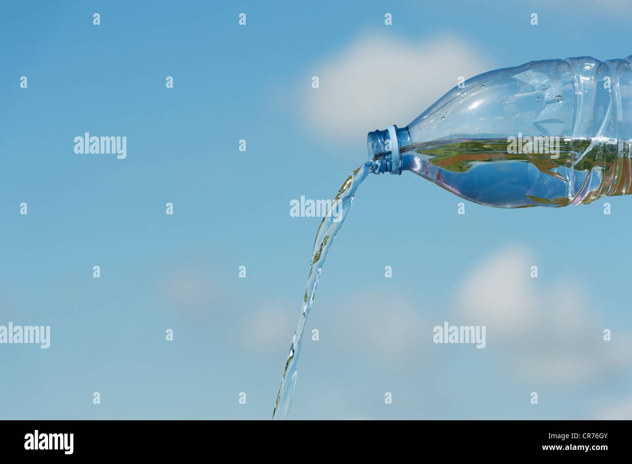 Verser de l'eau potable à partir d'une bouteille en plastique contre un ciel bleu Banque D'Images
