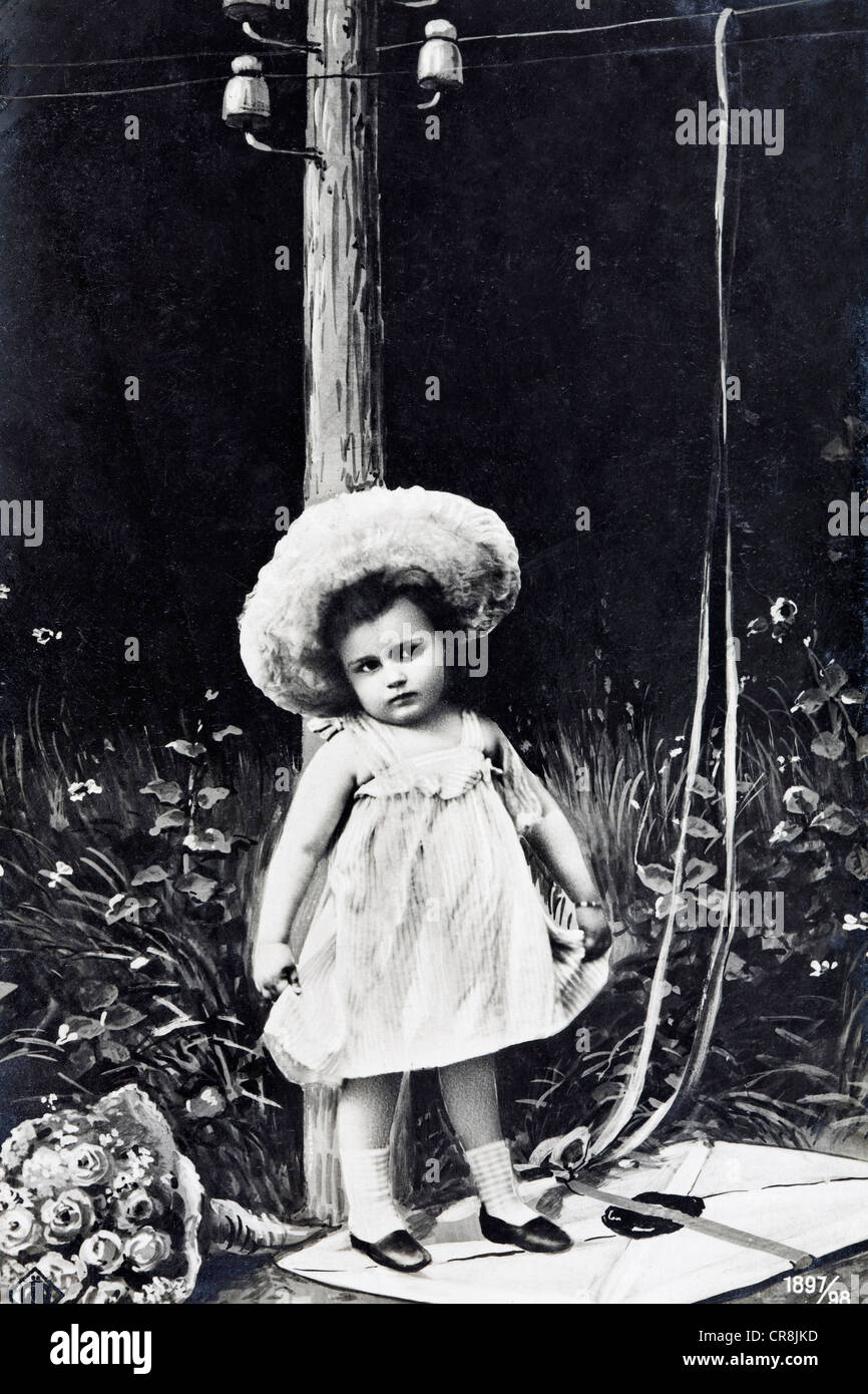 Cute little girl debout sur une lettre avec un bouquet de fleurs, carte postale historique, vers 1900, le kitsch Banque D'Images