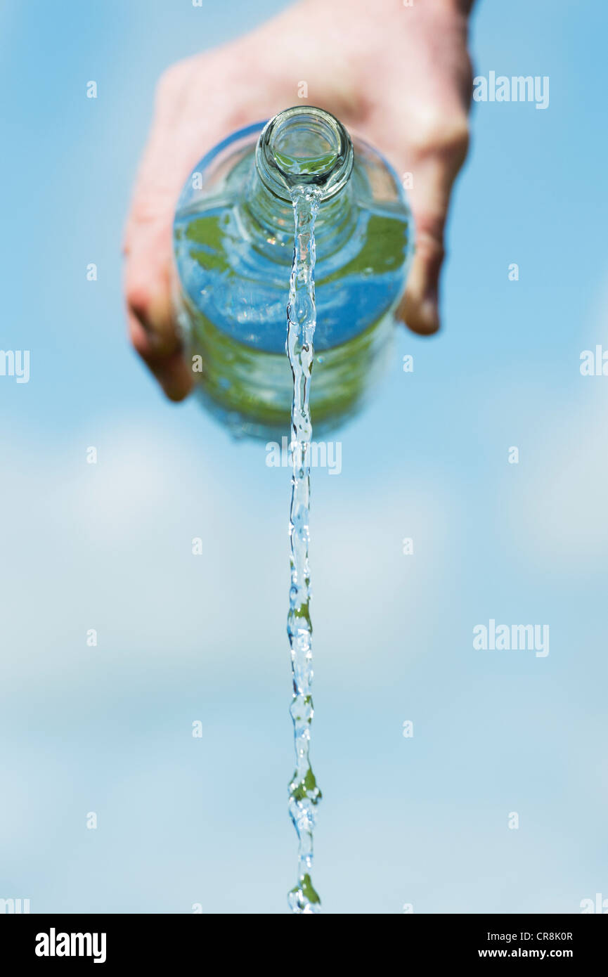 Verser de l'eau potable à partir d'une bouteille de verre contre un ciel bleu Banque D'Images