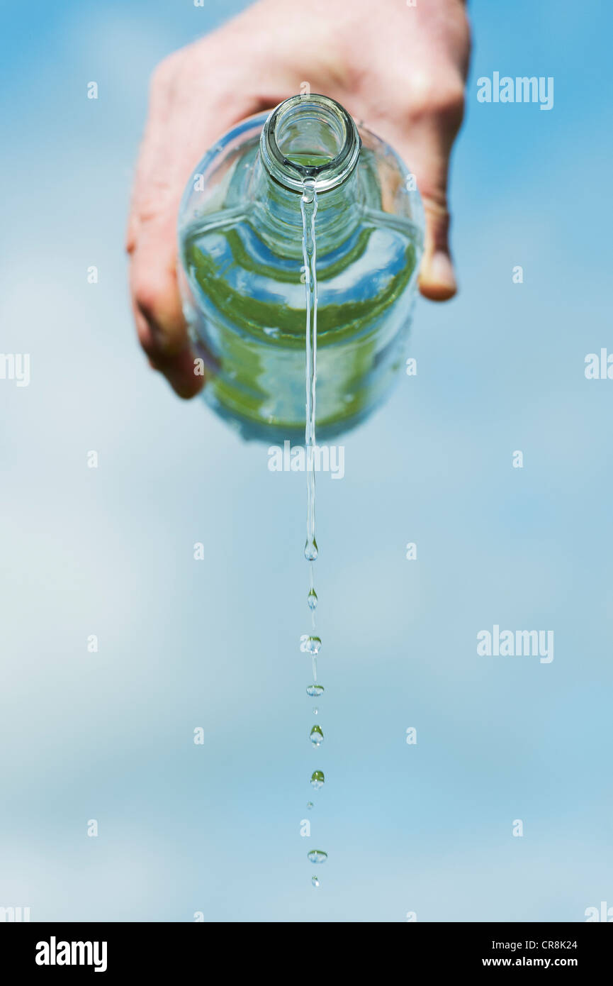 Verser de l'eau potable à partir d'une bouteille de verre contre un ciel bleu Banque D'Images
