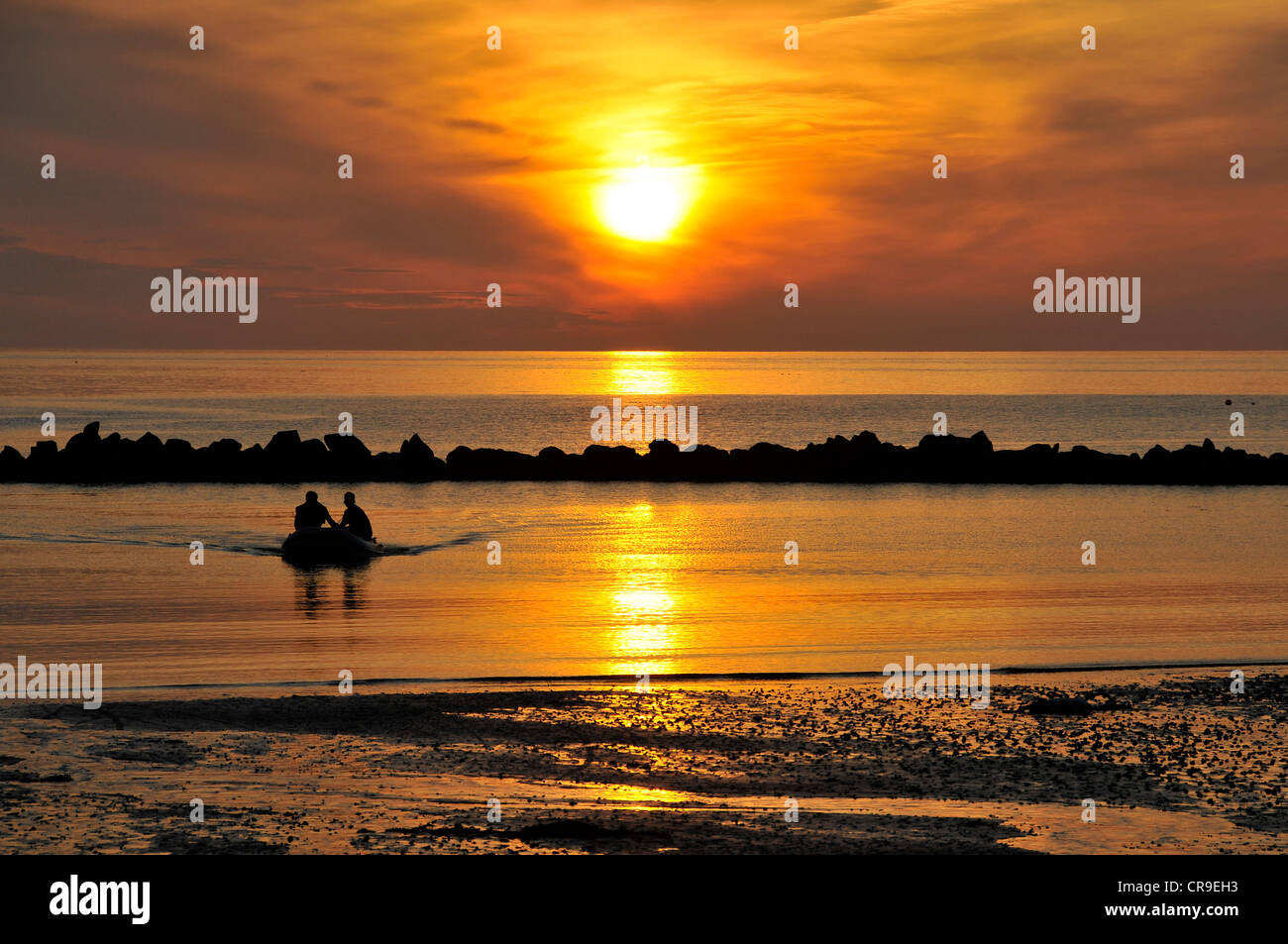 Les pêcheurs débarquant sur bois de Combe Martin, Devon, silhouetté contre le ciel orange vif de coucher du soleil. Banque D'Images