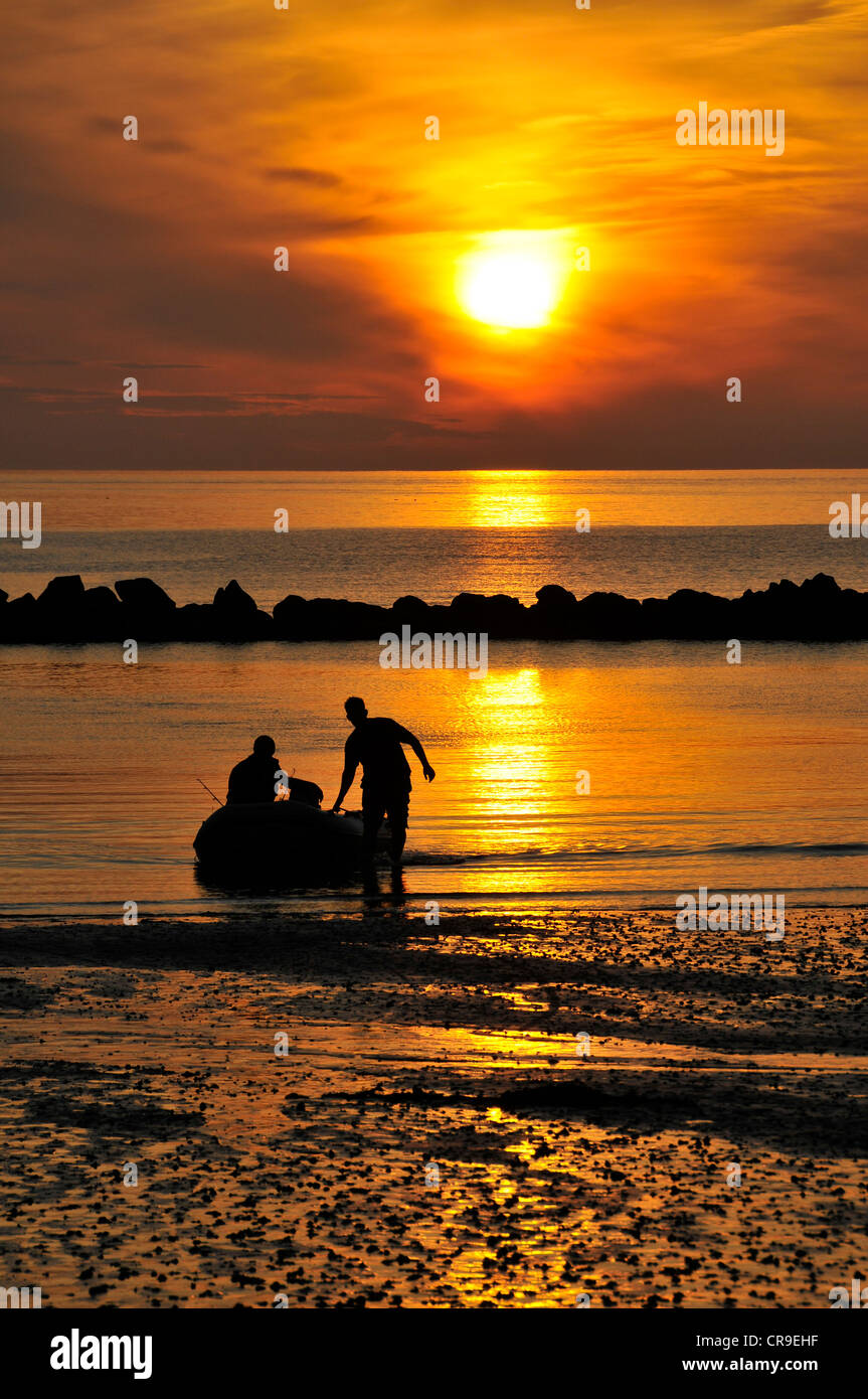 Les pêcheurs débarquant sur bois de Combe Martin, Devon, silhouetté contre le ciel orange vif de coucher du soleil. Banque D'Images