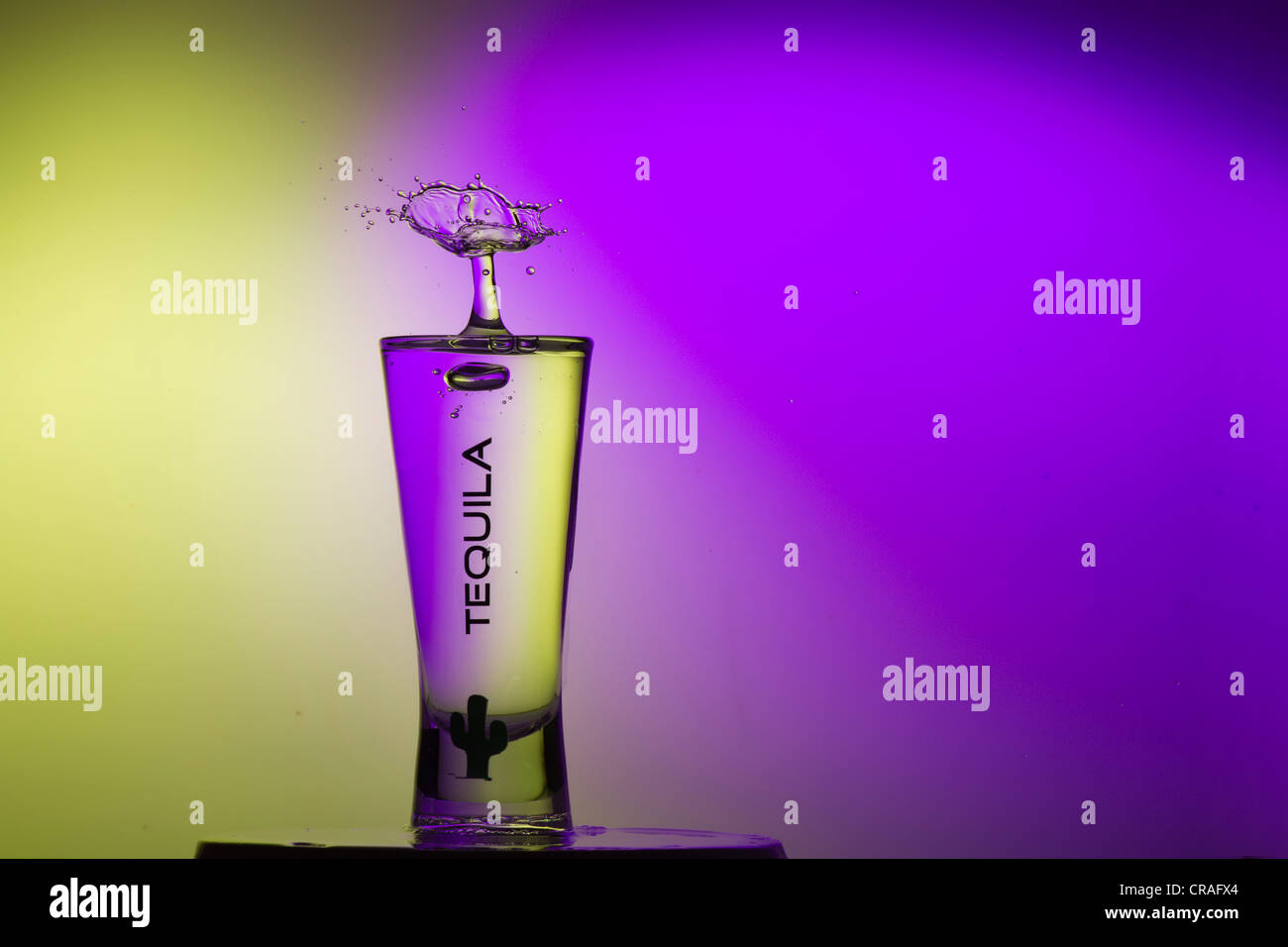 Drop bizarre sculpture sur un verre de tequila, l'éclairage violet et jaune Banque D'Images